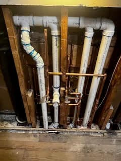 Exposed plumbing pipes in a wall, featuring PVC and copper materials for water supply lines.
