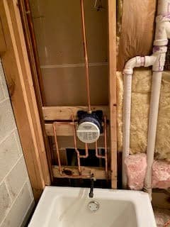 Plumbing installation featuring copper pipes and a water meter in a basement renovation.