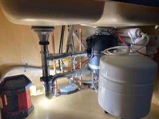 Under-sink plumbing system with garbage disposal, water tank, and illuminated work area.