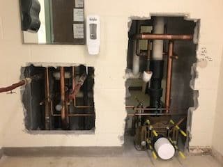Exposed plumbing and pipes in a wall cavity, showcasing copper and PVC installations.