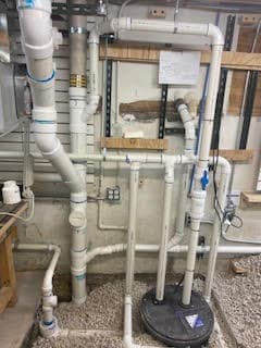 PVC plumbing system with pipes and fittings in a basement work area.